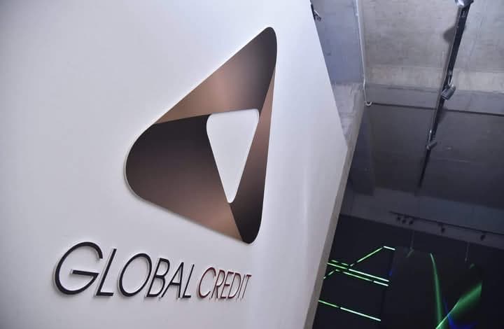 Logo Global Credit composé d'un triangle marron sur un mur blanc, vue en contre-plongée.
